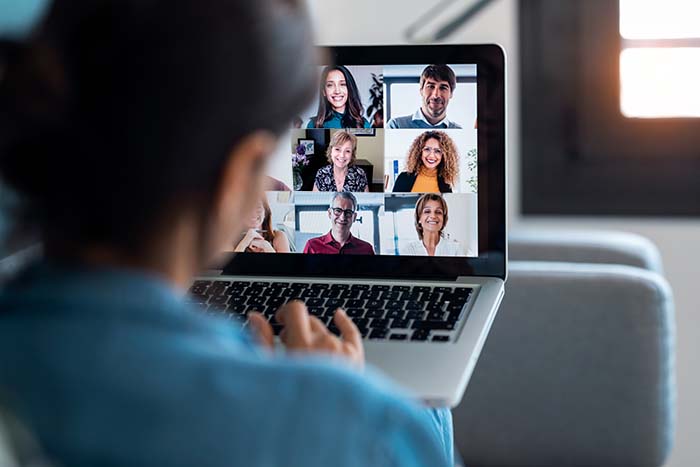 Back view of business woman speaking on video call with diverse colleagues on online briefing with laptop on sofa at home.